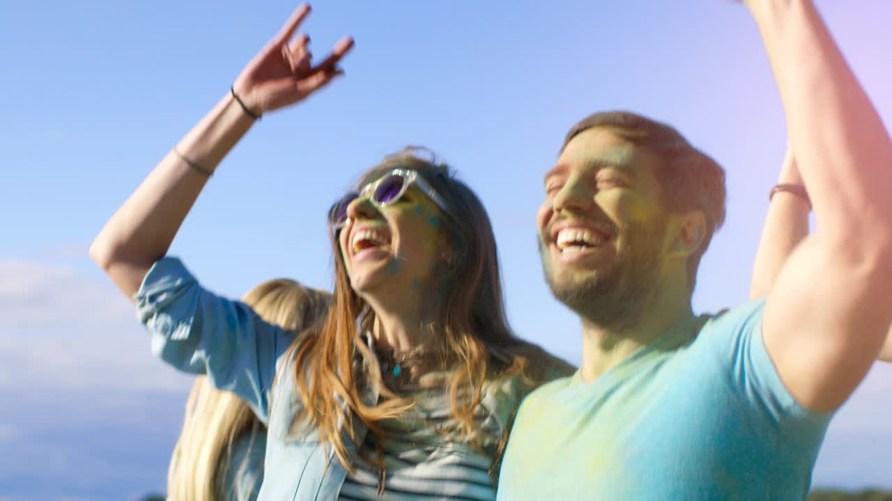 retrato de una pareja feliz cubierta de colorido polvo bailando en el festival de holi. la gente en el fondo se divierten lanzando polvo de holi