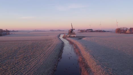 Flying-over-small-ditch-with-swimming-birds-towards-dutch-windmill,-aerial