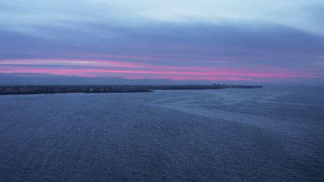 Purple-cloudy-sunset-above-Reykjavik-peninsula-in-Iceland,-low-light-aerial