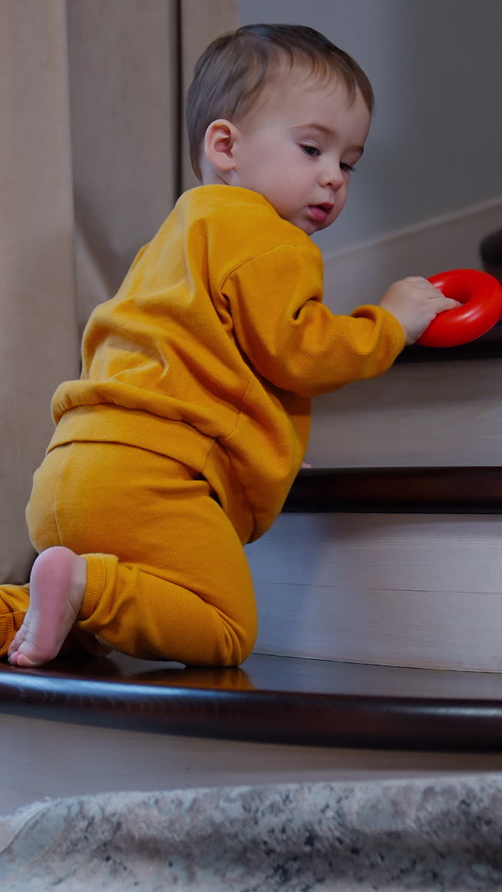 Beautiful baby plays on the stairs indoors. Lovely toddler throws the ring from toy pyramid and goes to get it back. Vertical video