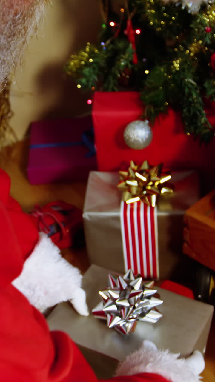 santa claus colocando una caja de regalos cerca del árbol de navidad