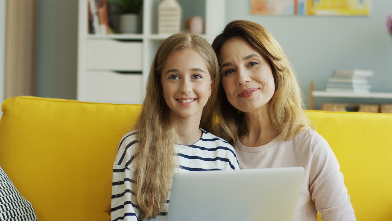 Blonde Mother And Daughter Sitting On Sofa While Watching Something On Computer