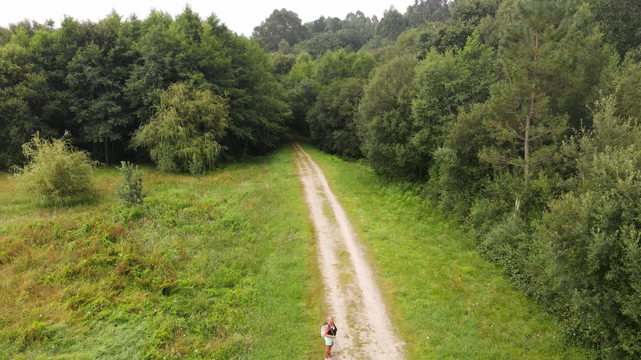 gruppo di persone, donne e uomini, che tengono bastoni che camminano su un sentiero forestale