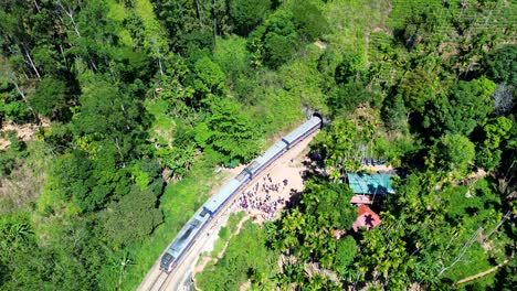 aerial drone scenic view of train with locomotive carriages travelling along railway line entering into tunnel with people standing near ella sri lanka asia