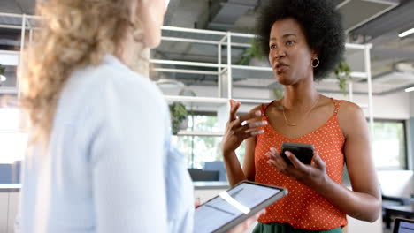 diversas colegas creativas en discusión usando tabletas y teléfonos inteligentes en la oficina, en cámara lenta