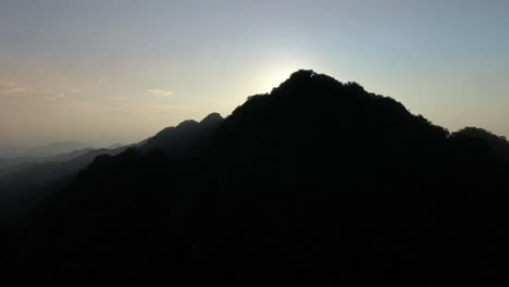 aerial reveal shot of dark mountain silhouette and golden sunset lighting in background