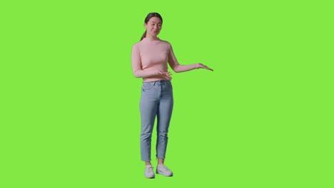 full length shot of woman presenting or demonstrating item against green screen smiling at camera