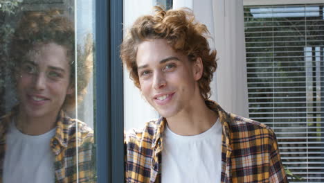 portrait of happy caucasian man looking through window at home, slow motion