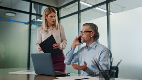 Nervous-businessman-talking-smartphone-at-office.-Stressed-couple-working-laptop