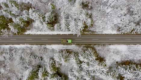 Following-a-green-lorry-by-drone-from-above,-driving-through-a-winter-landscape-as-top-shot-in-4K