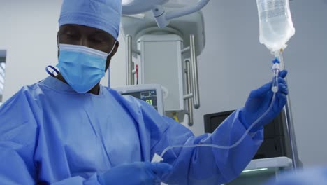 African-american-male-surgeon-wearing-protective-clothing-prepating-drip-in-operating-theatre