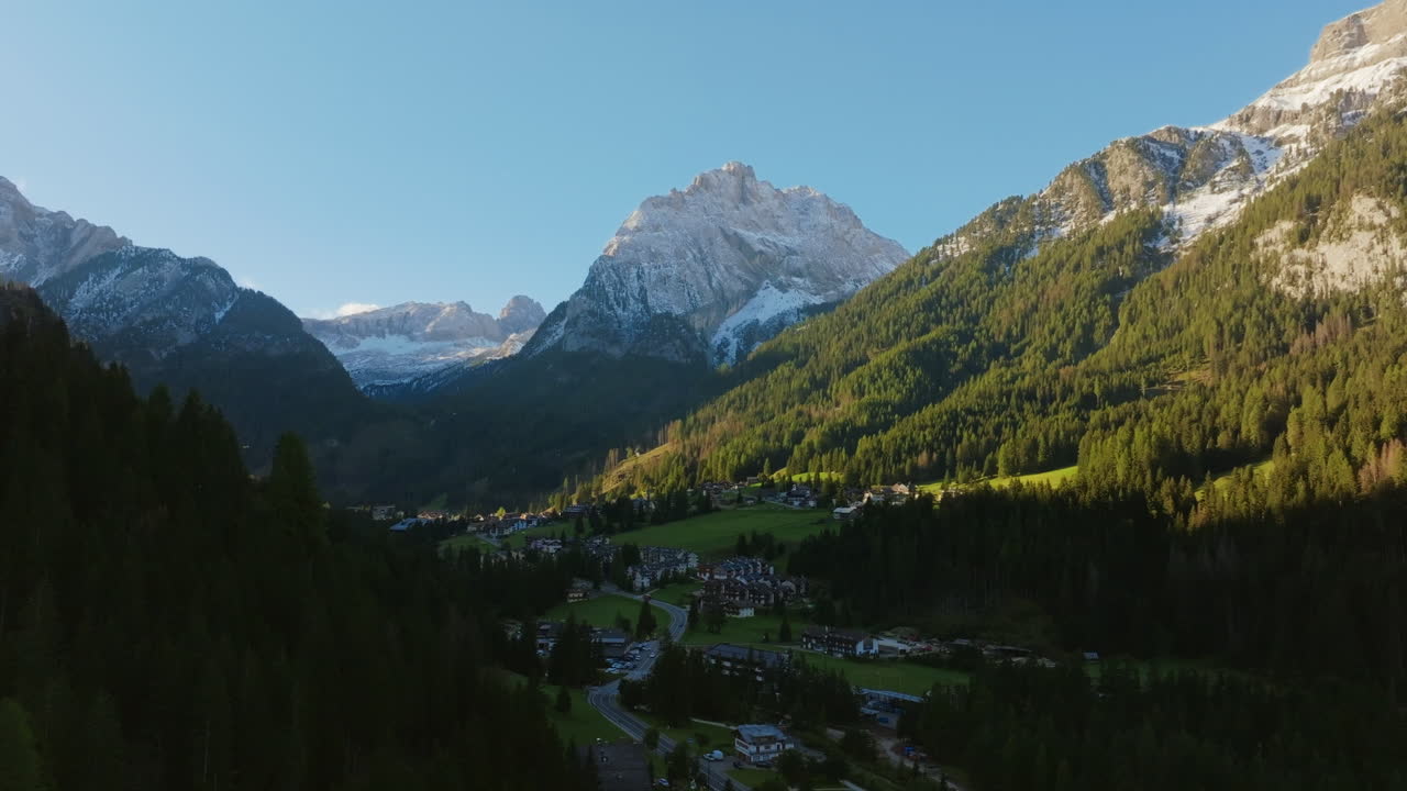 Aerial footage of Piccolo Vernel, mountain in the Marmolada Range of the Dolomites in Italy bathed in the morning light with a small town in the foreground.