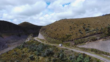 aerial dolly-in shot following a car navigating a winding dirt road in the vast ecuadorian paramo. the vehicle moves deeper into the highlands, surrounded by rugged mountains and untouched wilderness.