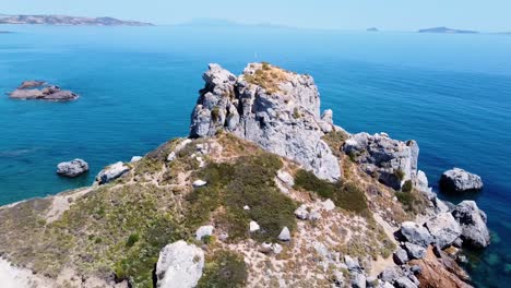 Cinematic-aerial-shot-of-a-rock-formation-in-a-paradisiacal-greek-island-with-a-small-church-on-it