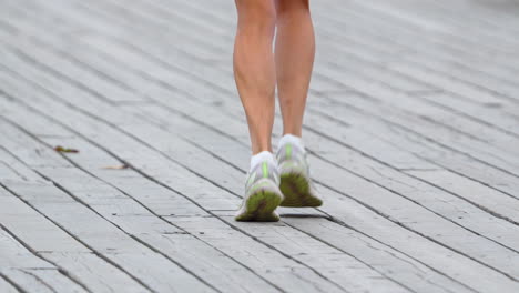 A-woman-in-light-colored-sports-shoes-runs-on-a-wooden-surface-made-of-planks,-slow-motion,-tight-shot