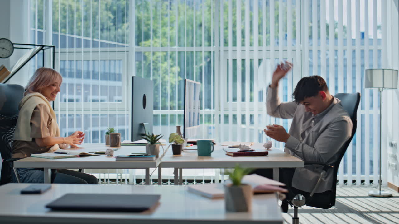 Playful colleagues having fun at workplace. Happy couple throwing paper at break