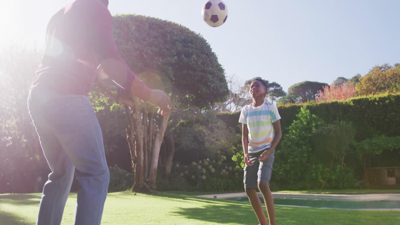 padre e hijo afroamericanos jugando al fútbol juntos en el jardín en un brillante día soleado