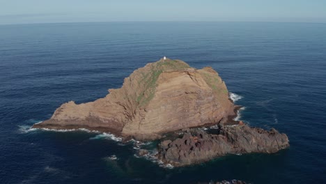 Gran-Roca-En-Un-Sereno-Océano-Turquesa-Con-Un-Pequeño-Faro-En-La-Parte-Superior