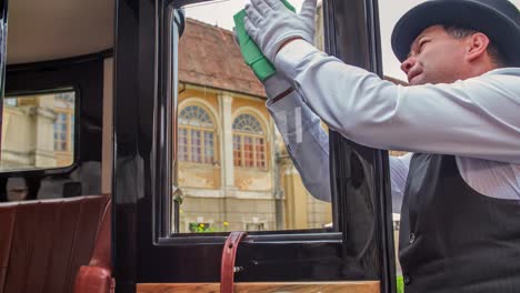 chauffeur gently polishing window of vintage car