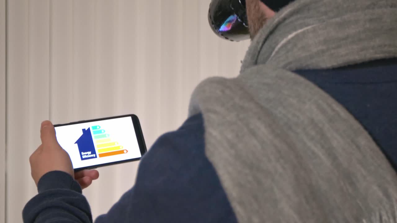 мужчина пьет кофе, держа в руках мобильный телефон с приложением по энергосбережению на экране