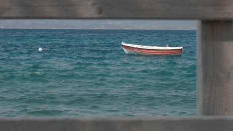 Slow-travelling-of-a-small-boat-moored-in-the-greek-coast-framed-with-a-wooden-balaustrade