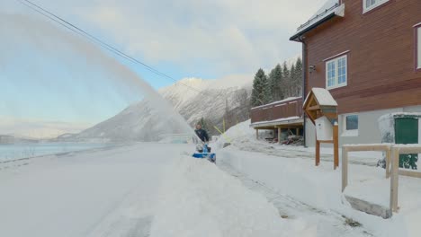 male removing hard compact snow with snow blower on a cold sunny winter day with a scenic landscape