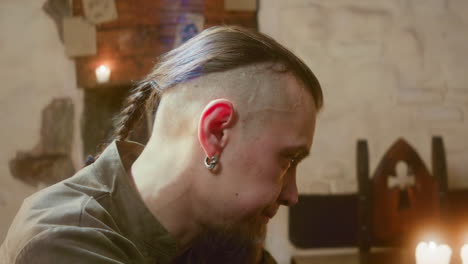 upset man nods head in tavern closeup. pensive guy with braided hair drowns sorrows in wine in medieval inn. guest rests in pub after bad day