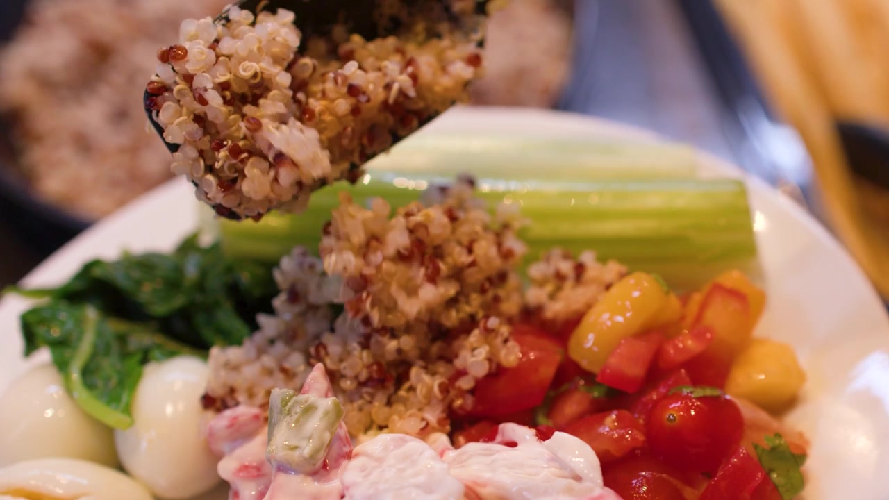 Primo piano di quinoa cotta servita con un cucchiaio su un piatto con verdure fresche e uova.