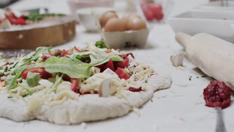un primer plano de queso y verduras en la masa de pizza con equipos de cocina en el mostrador, en cámara lenta.