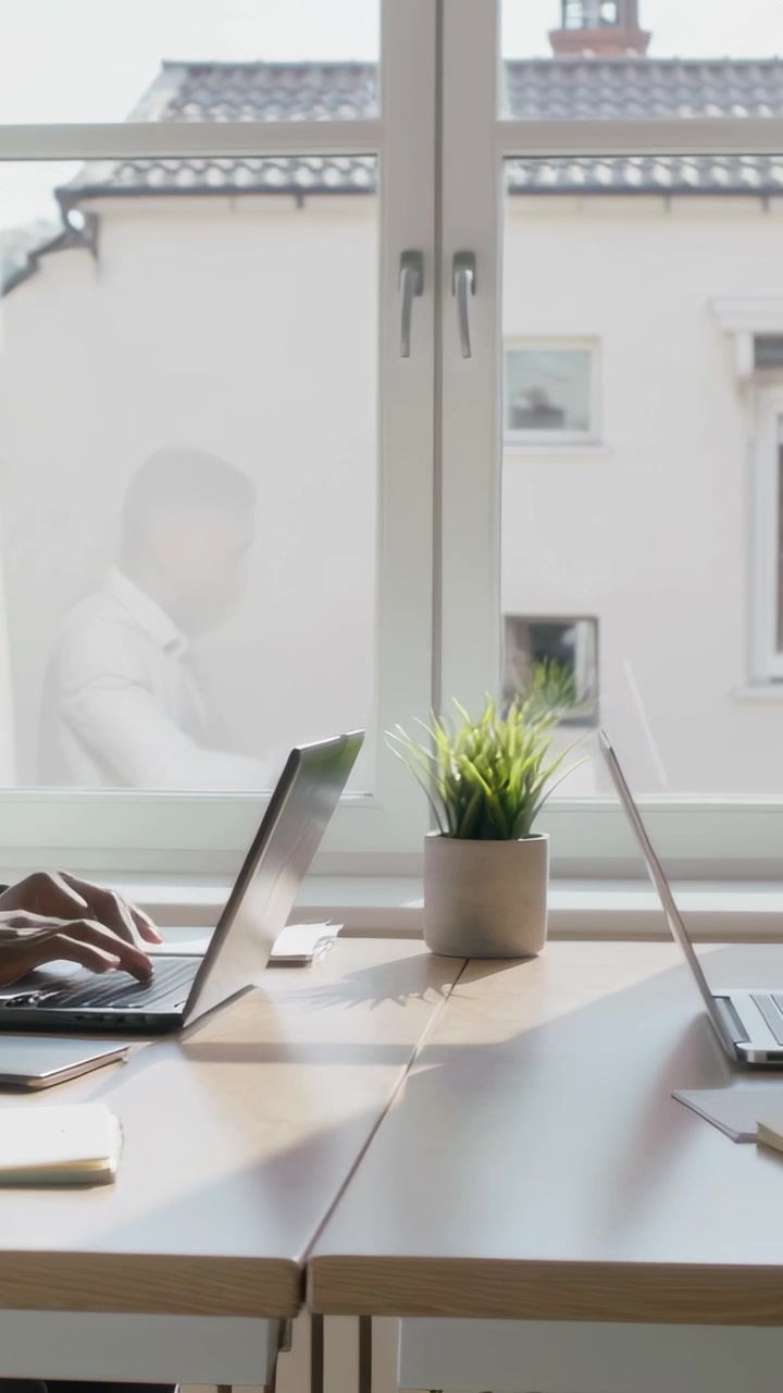 Video verticale: Panoramica che mostra un uomo in camicia che digita al laptop in ufficio, mani che appaiono, spazio per il testo.