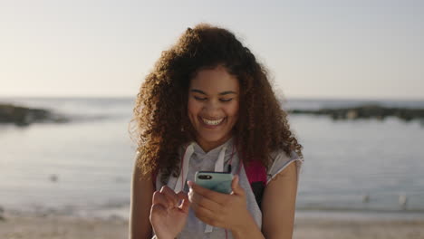 Porträt-Einer-Gemischtrassigen-Frau-Mit-Krausem-Haar,-Die-Einen-Sonnigen-Tag-Am-Strand-Genießt-Und-Lächelt-Und-SMS-Schreibt