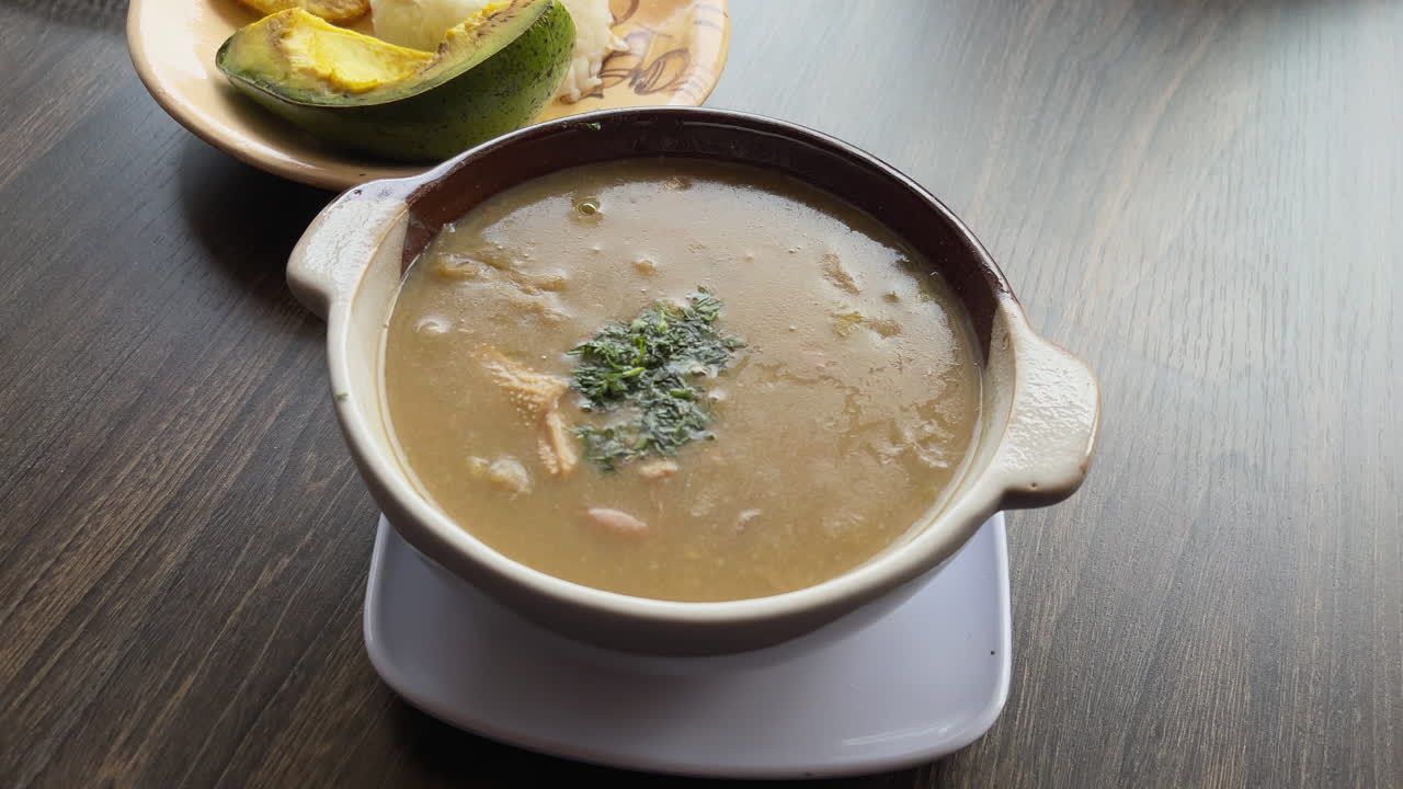 Classic ajiaco soup served hot with avocado and rice sides