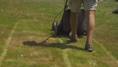 back view of unrecognizable man cutting grass with push lawn mower