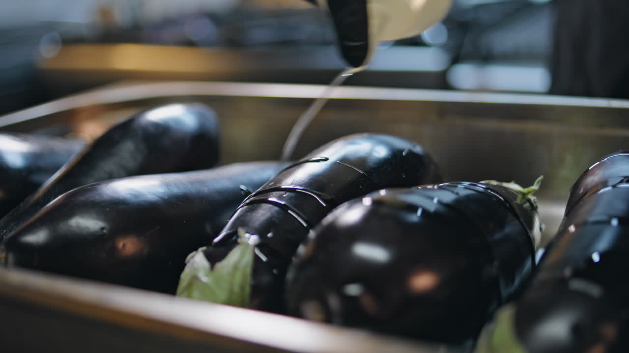 Chef pouring oil eggplants in tray preparing dish closeup. Professional hands