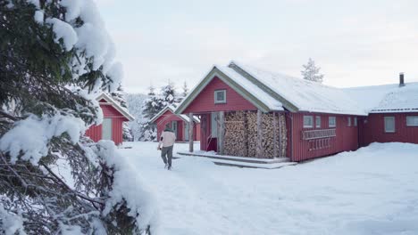 man with his dog walking in the snowy ground with traditional cabins at winter in norway