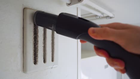 man cleaning off the dust from an air vent with a vacuum cleaner