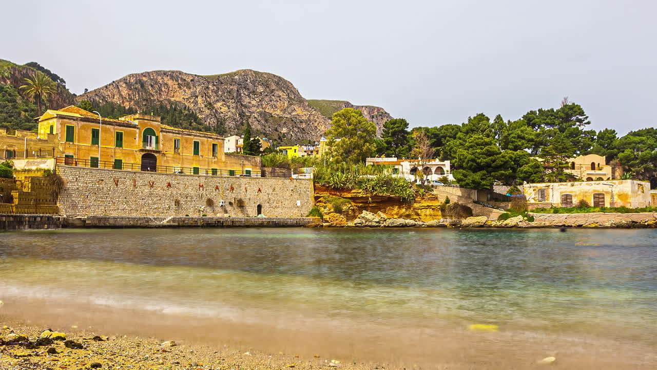 Timelapse, small gentle bay overlooking stone wall, old buildings in Sicily