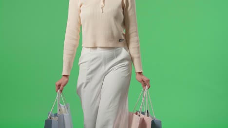 mujer de compras asiática con bolsas de compras sonríe y camina frente a la pantalla verde