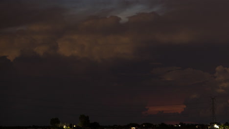 Flashing-electric-storm-over-pink-red-setting-clouds-over-a-setting-sun-horizon