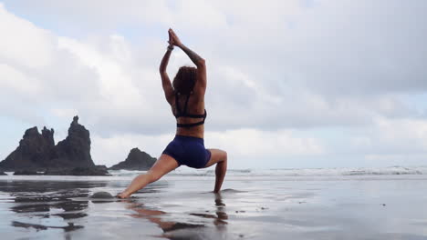 capturada en cámara lenta, una mujer joven y delgada se dedica al estiramiento y al yoga en la orilla del océano, su mirada fija en la distancia