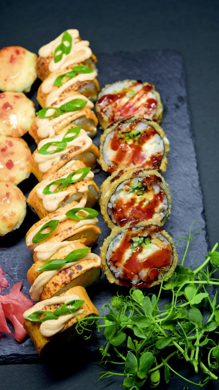 Roll di sushi con diversi condimenti e contorni su un piatto nero durante un pasto al ristorante