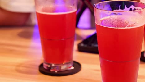 Close-up of red beverages in glasses on a wooden table with coasters.