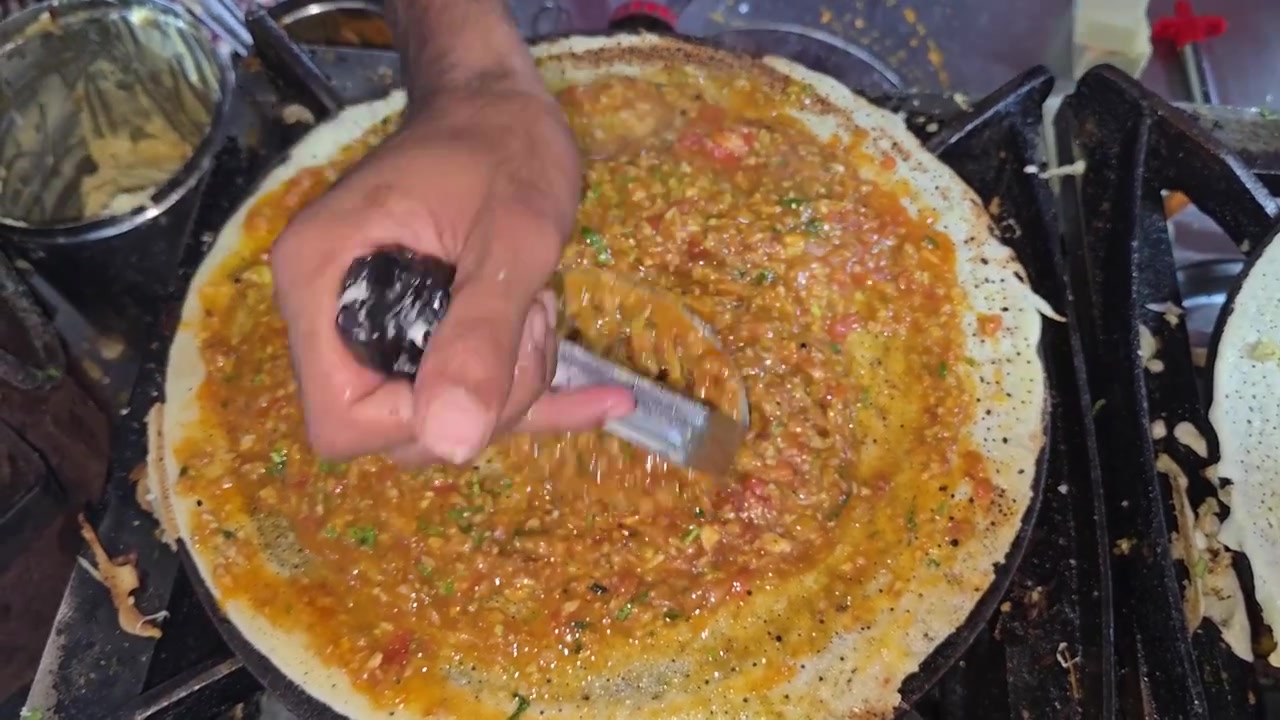 Bir Hint yemek tezgahında popüler bir Güney Hindistan yemeği hazırlarken, sıcak bir tavada çıtır bir dosa üzerine baharatlı patates masalayı ezen ve yayan bir sokak satıcısının yakın çekimi