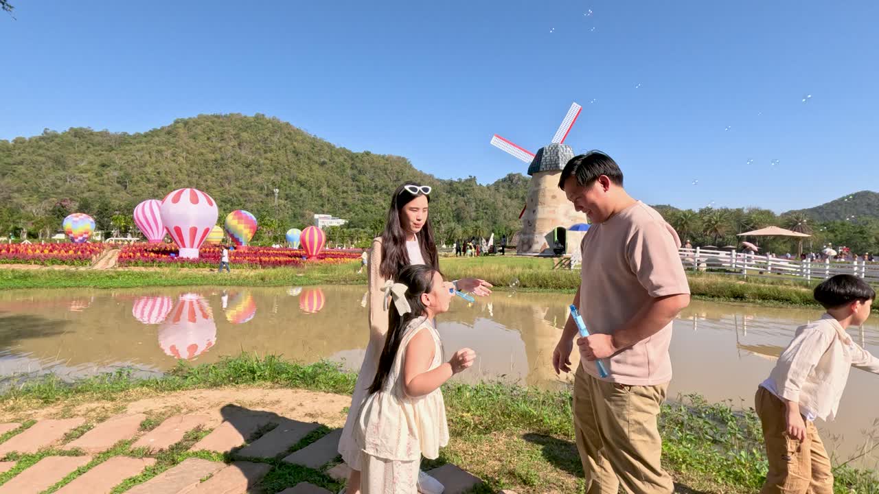 พ่อแม่และเด็กเป่าฟองสบู่ในสวนสาธารณะที่สวยงามซึ่งมีภูเขาและสระน้ำ