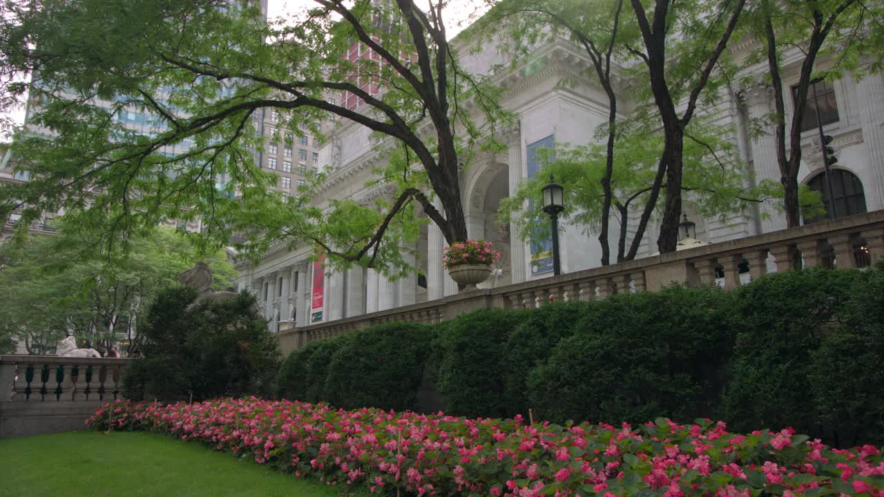 Beautiful garden against a classical NYC facade, vibrant flowers under lush trees. Overcast sky softens the light, adding serene elegance to an iconic urban setting