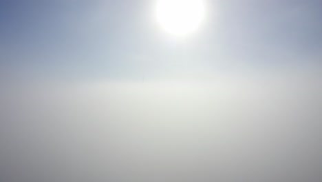 bright sun in blue sky with wind turbines in clouds