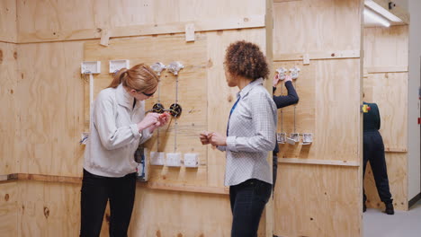 Female-Tutor-With-Trainee-Electricians-In-Workshop-Studying-For-Apprenticeship-At-College