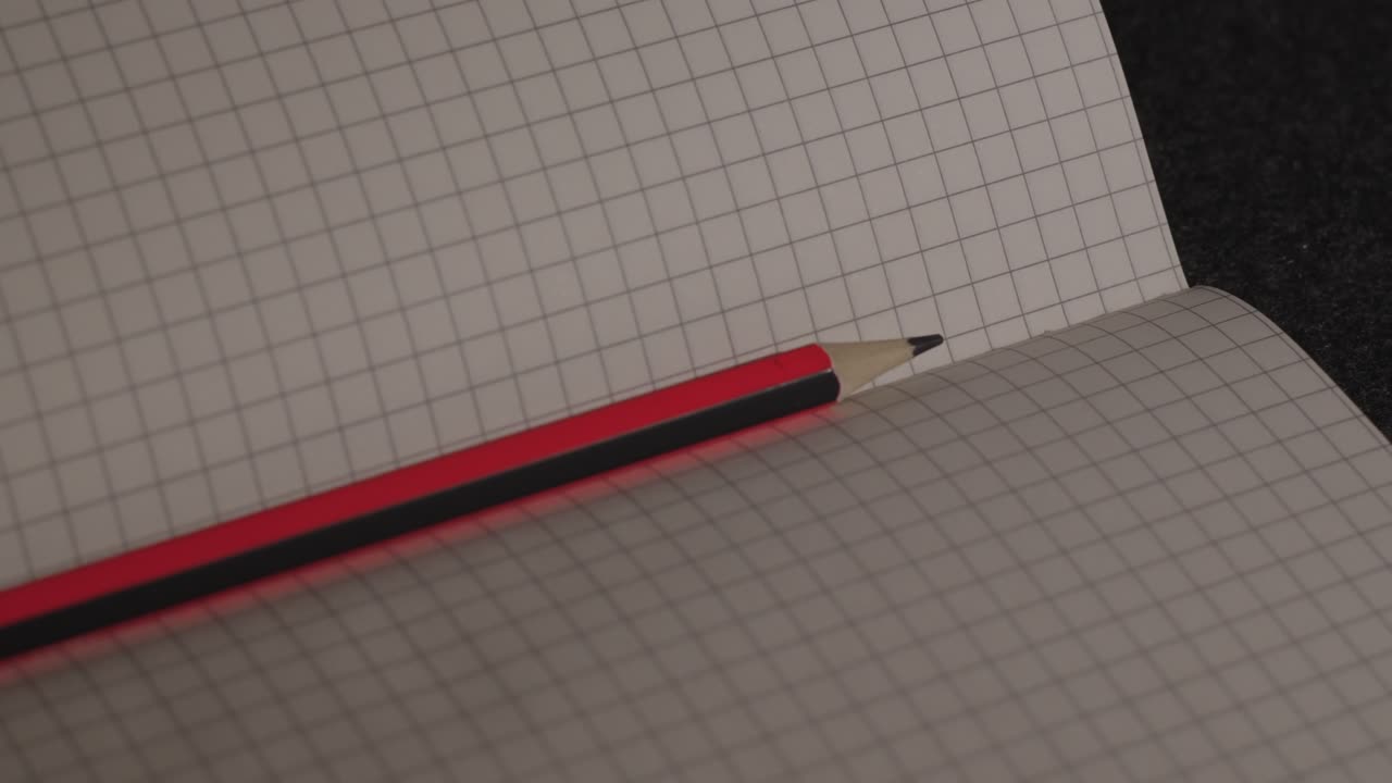 Primo piano di una matita rossa su un quaderno a quadretti con luce fioca.