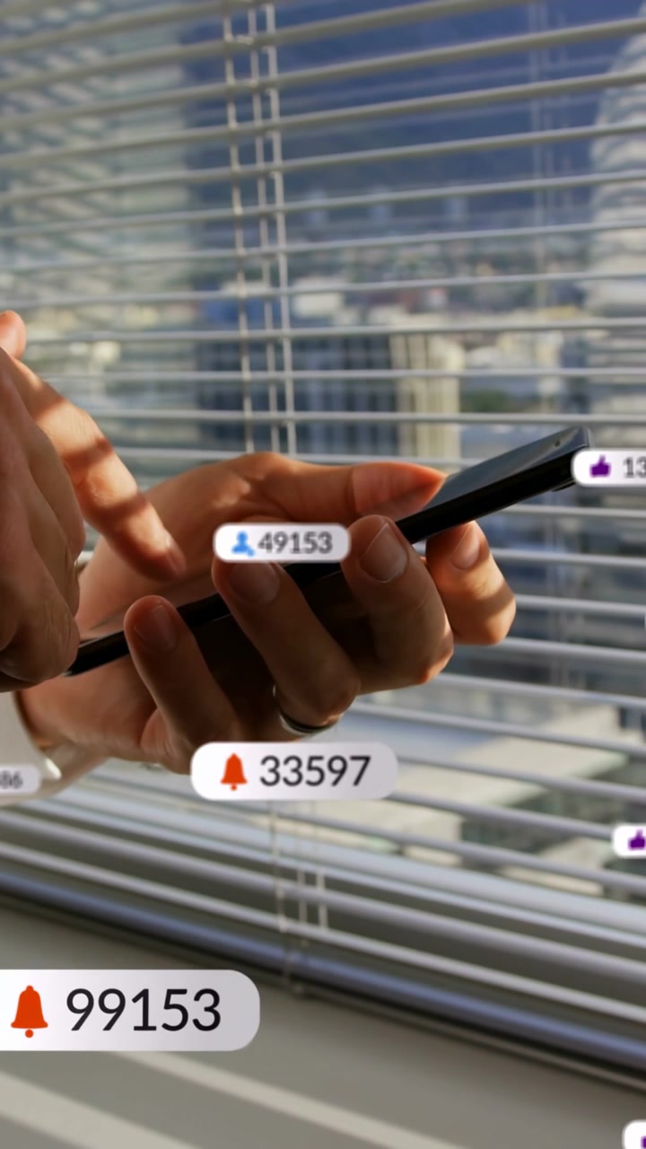 Vertical video: Man by blinds tapping phone, sending badges to rise then exit managing tech alerts