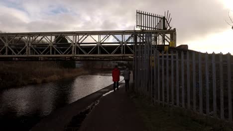 2-women-take-a-walk-along-by-the-former-industrial-canal-in-Stoke-on-Trent,-a-poverty-stricken-area-featuring-many-factories-in-ruins-along-by-the-canal